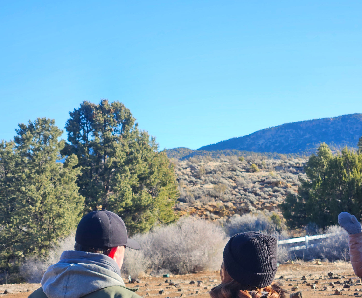 Two people standing outdoors with a scenic background of trees and mountains.